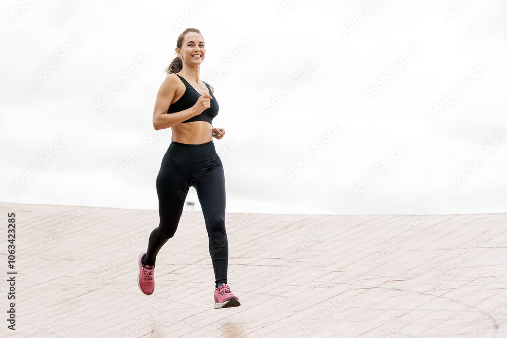 A Young Woman Enjoys Jogging on a Smooth Outdoor Track During a Cloudy Day, Demonstrating Fitness and Vitality A Young Woman Enjoys Jogging on a Smooth Outdoor Track During a Cloudy Day, Demonstrating Fitness and Vitality