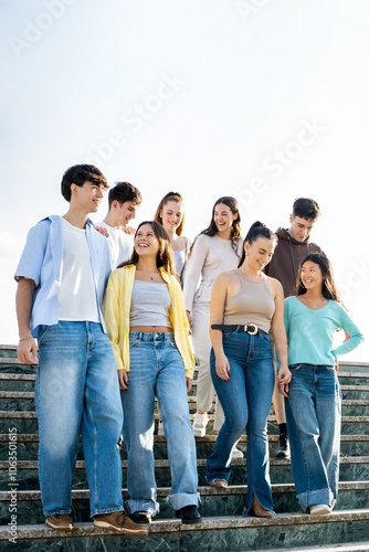 A group of 8 20-year-olds of different nationalities have fun in the streets of a city.The teenagers are going down some stairs while talking happily.Concept of youth groups in a city.