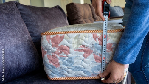 The female salesperson is measuring a mattress sample on a sofa, demonstrating it for the customer.