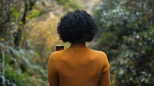 Back view of a woman with short curly black hair using a smartphone in a natural setting. This image captures the essence of the moment, with ample space for photo style elements.