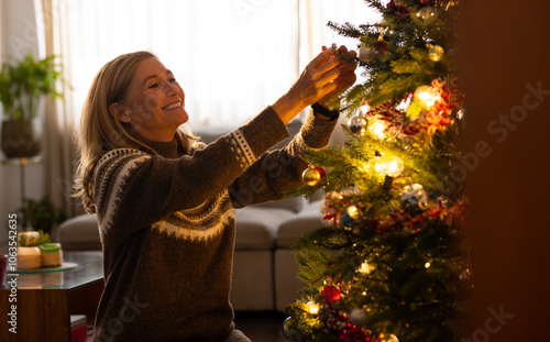 Smiling senior woman decorating Christmas tree with ornaments at home photo