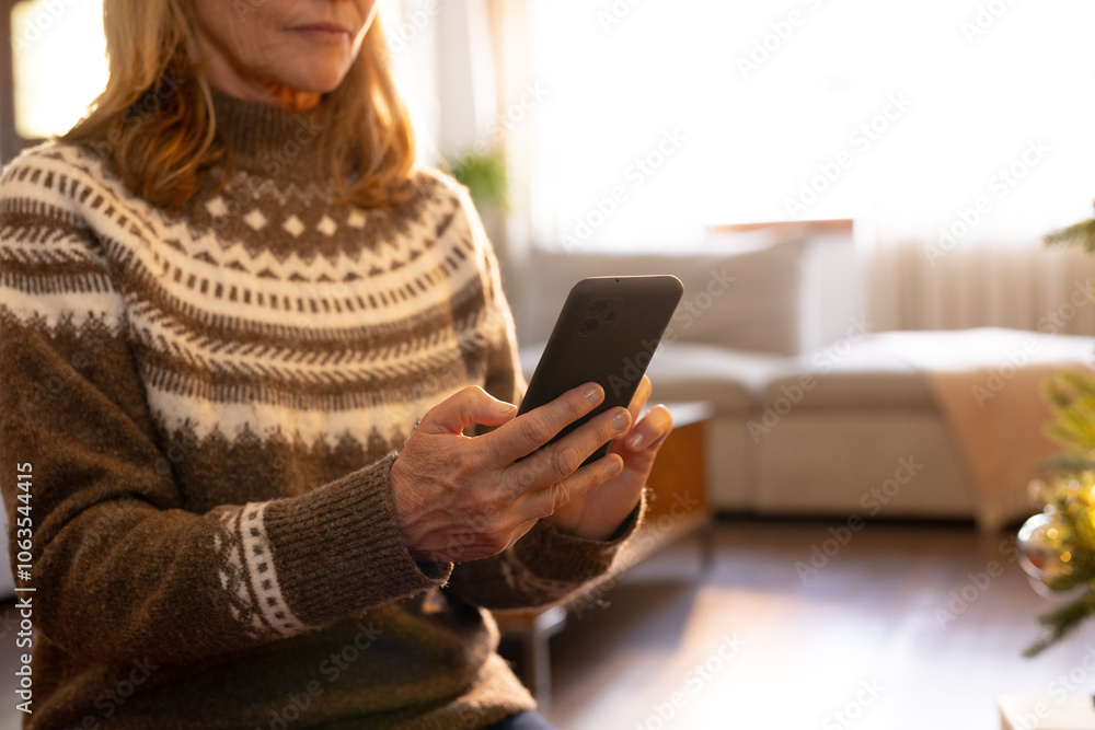 senior woman in cozy sweater using smartphone at home during Christmas senior woman in cozy sweater using smartphone at home during Christmas