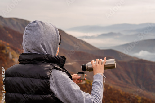 A happy traveler woman drinks a coffee or tea from a cup thermos bottle relaxing during a hike and enjoys the scenery in the mountains adventure travel.