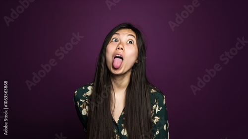 Woman with long hair playfully sticking out her tongue against a solid dark purple background, wearing a floral patterned top, playful and humorous vibe. photo