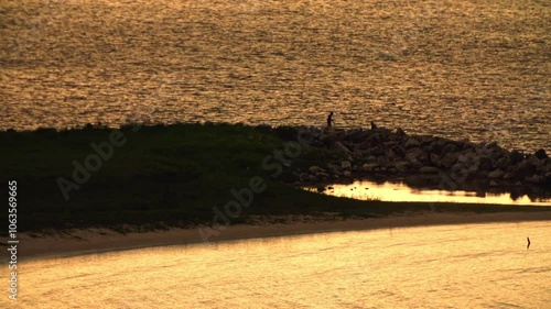 Telephoto of two fishermen on a rocky jetty with golden sunset light on the water of Montego Bay, Jamaica, with ambient sounds of the city