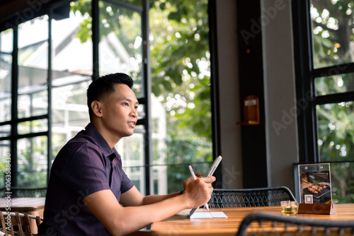 Young Professional Enjoying Remote Work in Cozy Cafe or Coffee Shop while using gadget