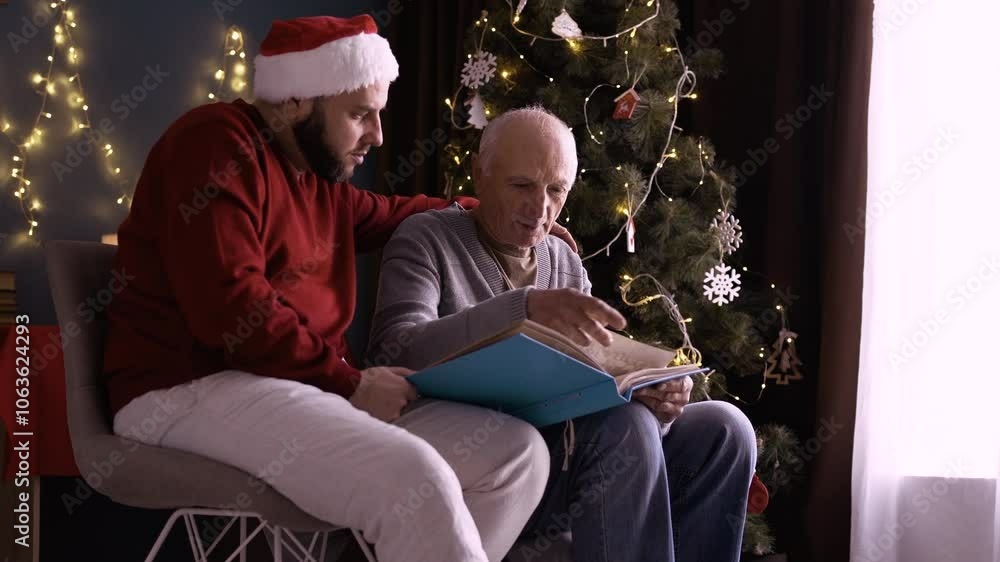 Father and son looking at photos in an old photo album reminiscing about the past on Christmas Eve in the living room of their home Father and son looking at photos in an old photo album reminiscing about the past on Christmas Eve in the living room of their home