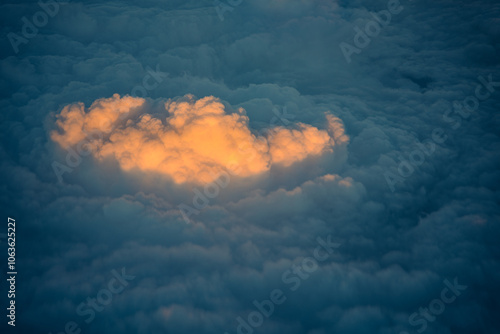 Clouds aerial view. Light in between darkness. Sun beam illuminating a cloud in warm tones against the cold dark blue cloudscape in the evening sky, as seen from above. Unique special moment. photo