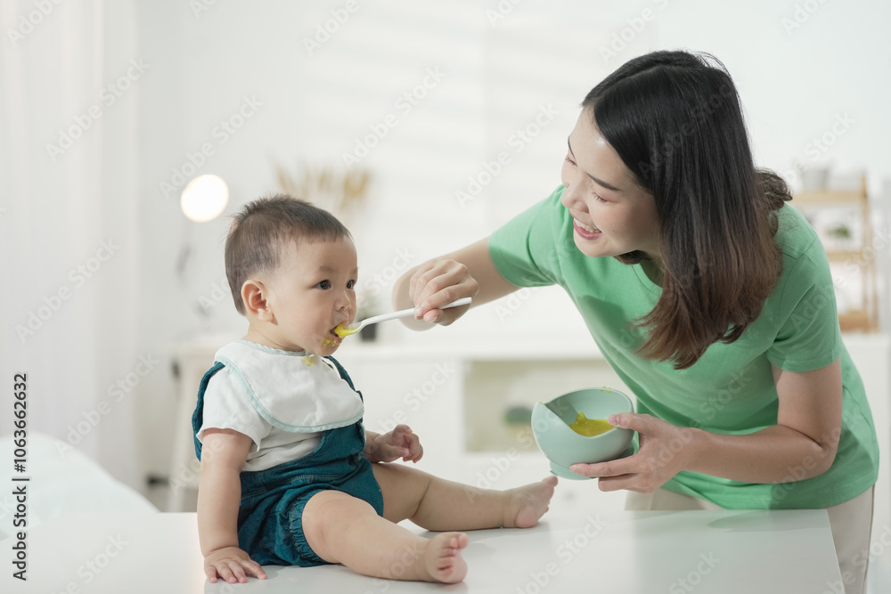 feeding time for baby. Mother lovingly feeds joyful toddler with spoon at home, maternal care. Charming little baby boy 6-8 months eating first food pumpkin from spoon with mom at home. feeding time for baby. Mother lovingly feeds joyful toddler with spoon at home, maternal care. Charming little baby boy 6-8 months eating first food pumpkin from spoon with mom at home.