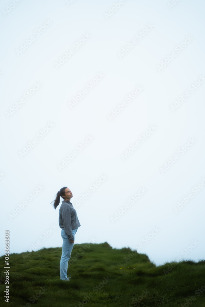 Woman standing in the middle of a cliff in a foggy day Woman standing in the middle of a cliff in a foggy day