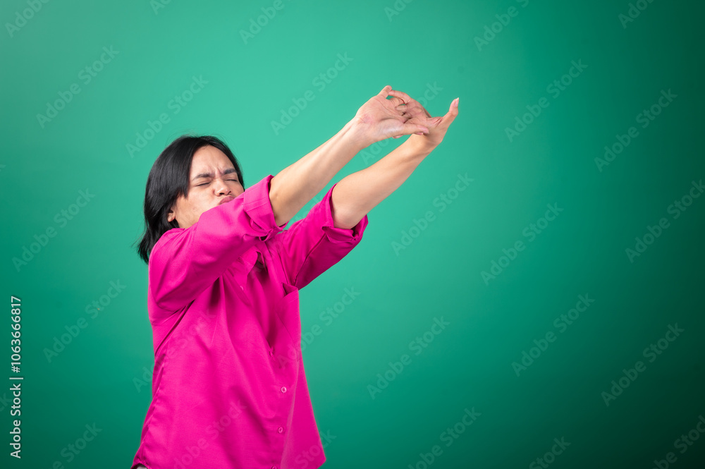 Asian woman in a bright pink shirt against a green background appears to be yawning, with arms stretched out in a gesture of tiredness or fatigue. Her facial expression body language sleepiness. Asian woman in a bright pink shirt against a green background appears to be yawning, with arms stretched out in a gesture of tiredness or fatigue. Her facial expression body language sleepiness.