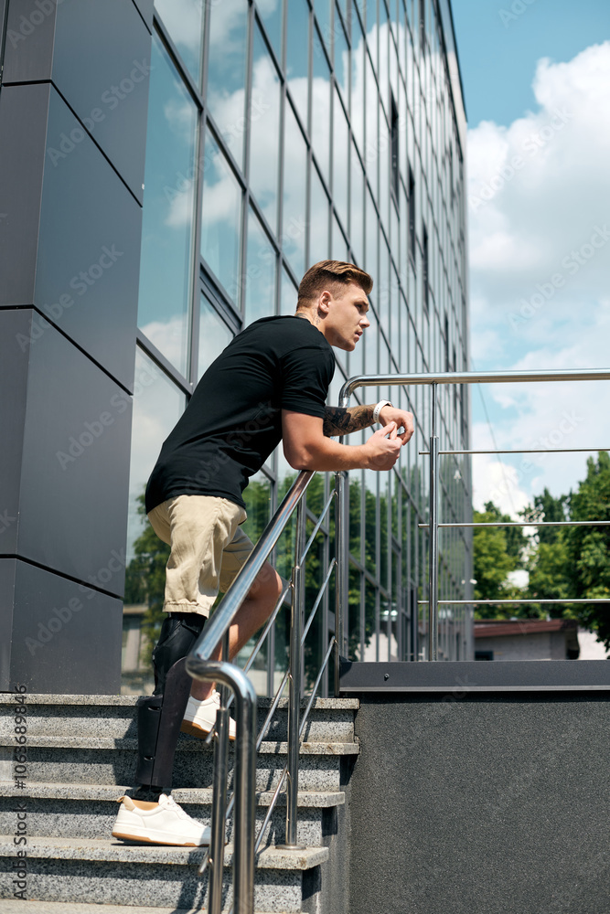 A young professional with a prosthetic leg leans against a railing, contemplating his workday in the office. A young professional with a prosthetic leg leans against a railing, contemplating his workday in the office.