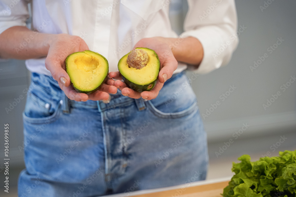 Close up of two halves of avocado in hands of female on a kitchen