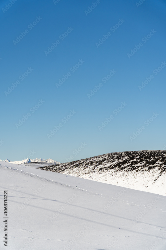 A vertical perspective of a snowy hill featuring rocky textures against a bright blue sky, highlighting the beauty of the winter landscape.