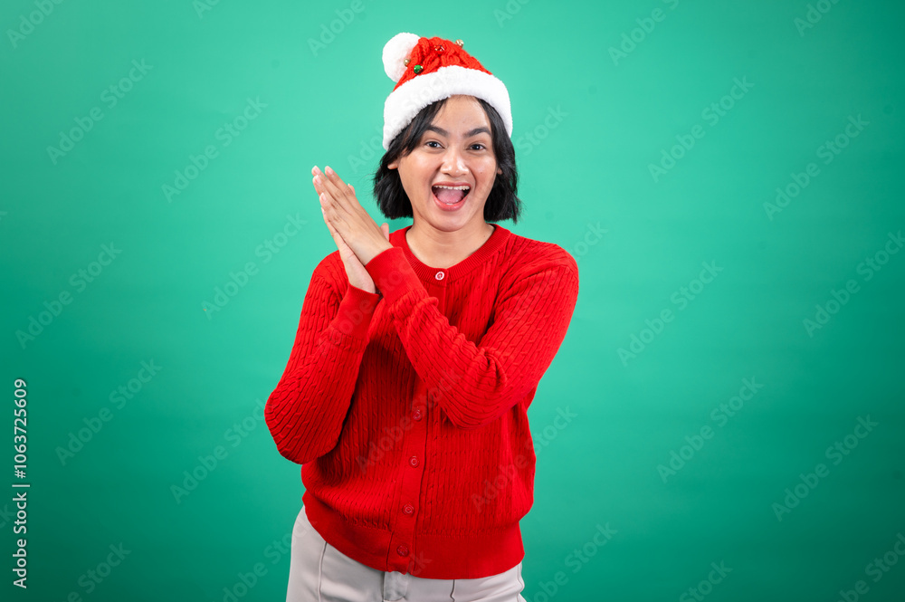 An Asian woman wearing a red sweater and Santa hat claps her hands with a joyful expression, conveying festive energy. She stands against a green background, An Asian woman wearing a red sweater and Santa hat claps her hands with a joyful expression, conveying festive energy. She stands against a green background,