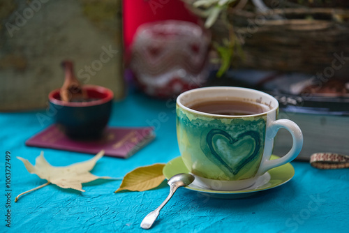 Table set on a turquoise tablecloth in the garden with tea, spices, candlelight, travel book and autumn leaves photo