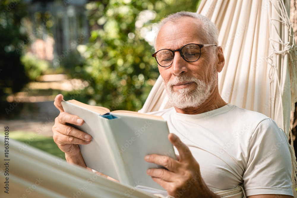 Concentrated dreamy senior elderly grandfather man relaxing resting in hammock while reading book