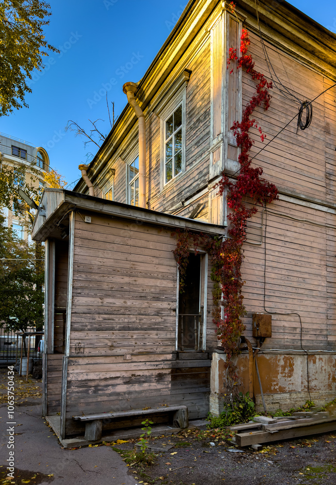 A rustic wooden house in Saint Petersburg is bathed in warm autumn sunlight, with vibrant red vines climbing its faded exterior. The sunlight accentuates the textures of the weathered wood, adding A rustic wooden house in Saint Petersburg is bathed in warm autumn sunlight, with vibrant red vines climbing its faded exterior. The sunlight accentuates the textures of the weathered wood, adding