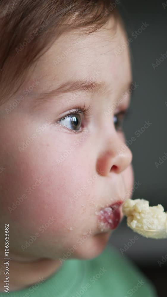 Beautiful baby with adorable cheeks is fed from spoon. Mom gives food to her child and kid takes it obediently. Close up. Blurred backdrop. Vertical video Beautiful baby with adorable cheeks is fed from spoon. Mom gives food to her child and kid takes it obediently. Close up. Blurred backdrop. Vertical video