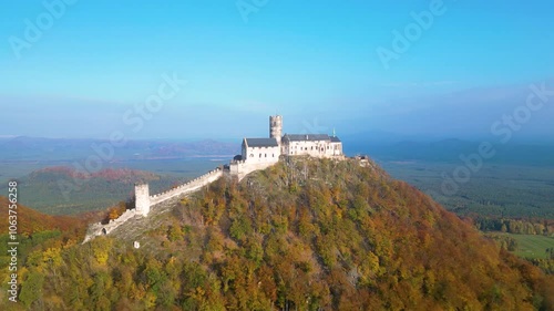 Witness the breathtaking view of Bezdez Medieval Castle as it is bathed in the warm glow of an autumn sunrise. The colorful foliage enhances the serene landscape. photo