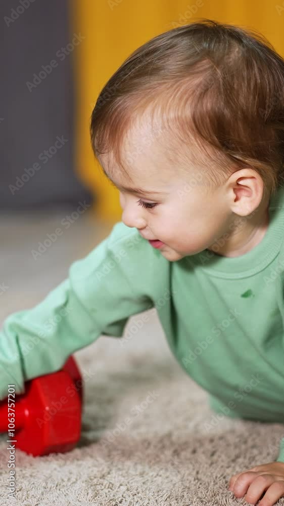 Curious toddler crawling up to the red dumbbells with interest. Adorable child takes one dumbbell and rolls it by the carpet. Blurred backdrop. Vertical video Curious toddler crawling up to the red dumbbells with interest. Adorable child takes one dumbbell and rolls it by the carpet. Blurred backdrop. Vertical video