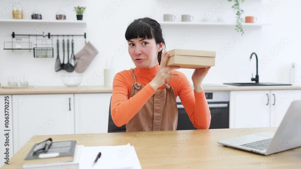 Caucasian female in 20s showcasing latest smartphone model from home office setting. Blogger presents tech product in modern kitchen workspace with laptop, notebook, and plant for online audience. Caucasian female in 20s showcasing latest smartphone model from home office setting. Blogger presents tech product in modern kitchen workspace with laptop, notebook, and plant for online audience.