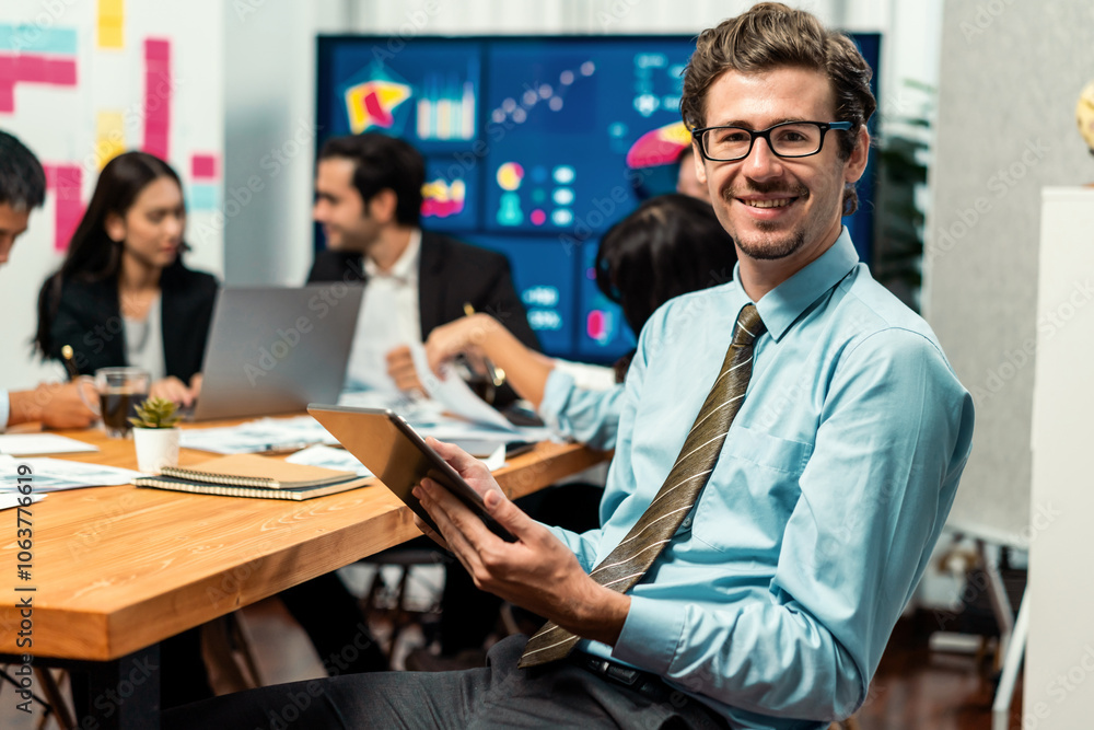 Portrait of businessman or analyst looking at camera with his colleague analyzing data analysis in dynamic business strategy investment planning meeting. Meticulous Portrait of businessman or analyst looking at camera with his colleague analyzing data analysis in dynamic business strategy investment planning meeting. Meticulous