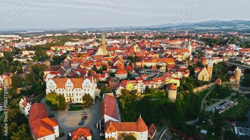 Drone wide-angle shot of Bautzen at sunset, capturing the historic cityscape bathed in warm, fading light. The scene highlights the town's iconic architecture and scenic skyline. Drone move left.