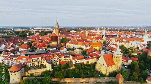 Drone wide-angle shot of Bautzen at sunset, capturing the historic cityscape bathed in warm, fading light. The scene highlights the town's iconic architecture and scenic skyline. Drone move left.