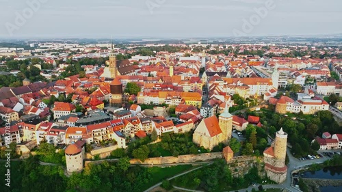 Drone wide-angle shot of Bautzen at sunset, capturing the historic cityscape bathed in warm, fading light. The scene highlights the town's iconic architecture and scenic skyline. Drone move right.