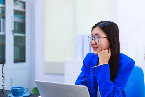 An Asian woman sits at her desk, surrounded by files , embodying dedication and professionalism in her work.