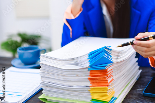 An Asian woman sits at her desk, surrounded by files , embodying dedication and professionalism in her work.