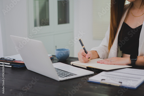 Asian businesswoman, focused , sits at ablack wooden table. Surrounded by notes , she strategizes her next move, embodying confidence and professionalism in her workspace. photo