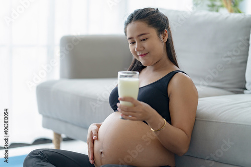 Asian female pregnant holding glass of milk in the living room, self care photo