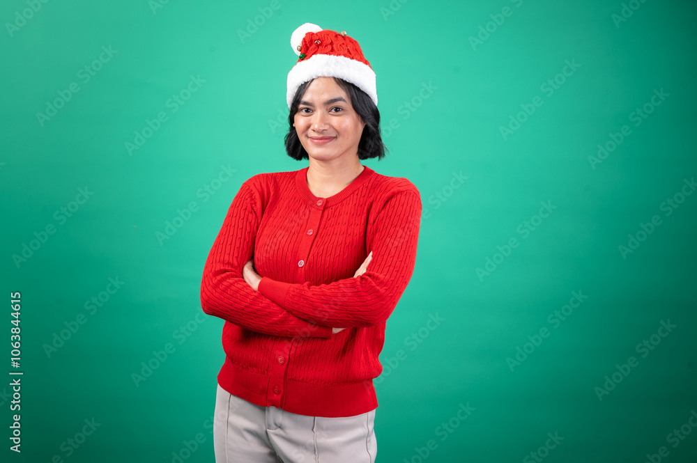 Asian woman wearing a red sweater and festive Santa hat stands confidently with her arms crossed against a green background, exuding a calm holiday spirit in a casual Christmas-themed Asian woman wearing a red sweater and festive Santa hat stands confidently with her arms crossed against a green background, exuding a calm holiday spirit in a casual Christmas-themed