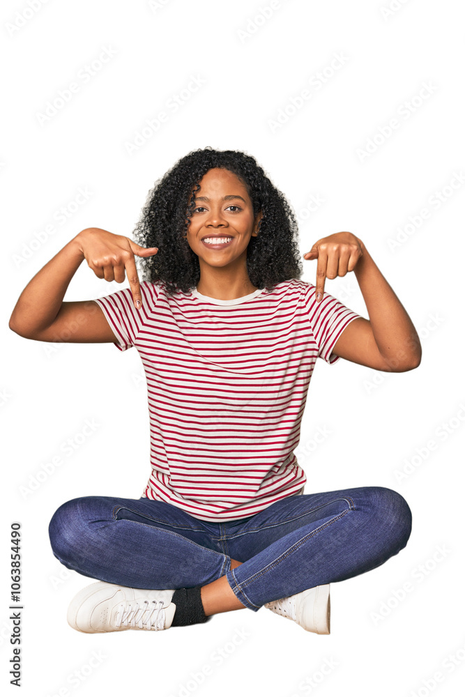 Obraz premium oung woman sitting on floor in studio points down with fingers, positive feeling.