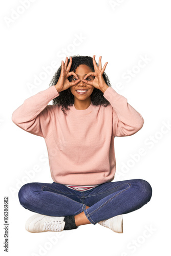 oung woman sitting on floor in studio showing okay sign over eyes