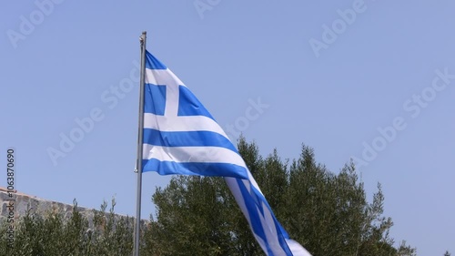 Greek flag waving in the wind, olive trees in the background.