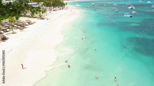 Aerial view of the snow-white tropical beach of the luxury hotel.Vacationers swim in the turquoise ocean water and sunbathe.Parked tourist catamarans for outdoor activities,romantic dates on vacation.