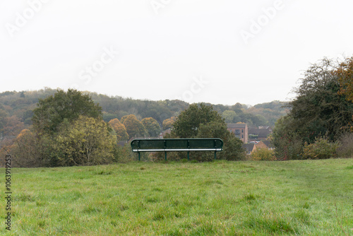 Park bench in front of a view of a forest and with houses. In South Oxhey playing fields Watford photo