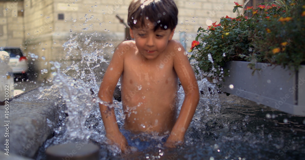 Obraz premium Young boy jumping into water, splashing playfully in a fountain, surrounded by flowers, in a historic European city square, captured in super slow motion at 800 fps