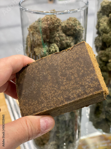 Holding a large block of hashish in front of jars of Marijuana 