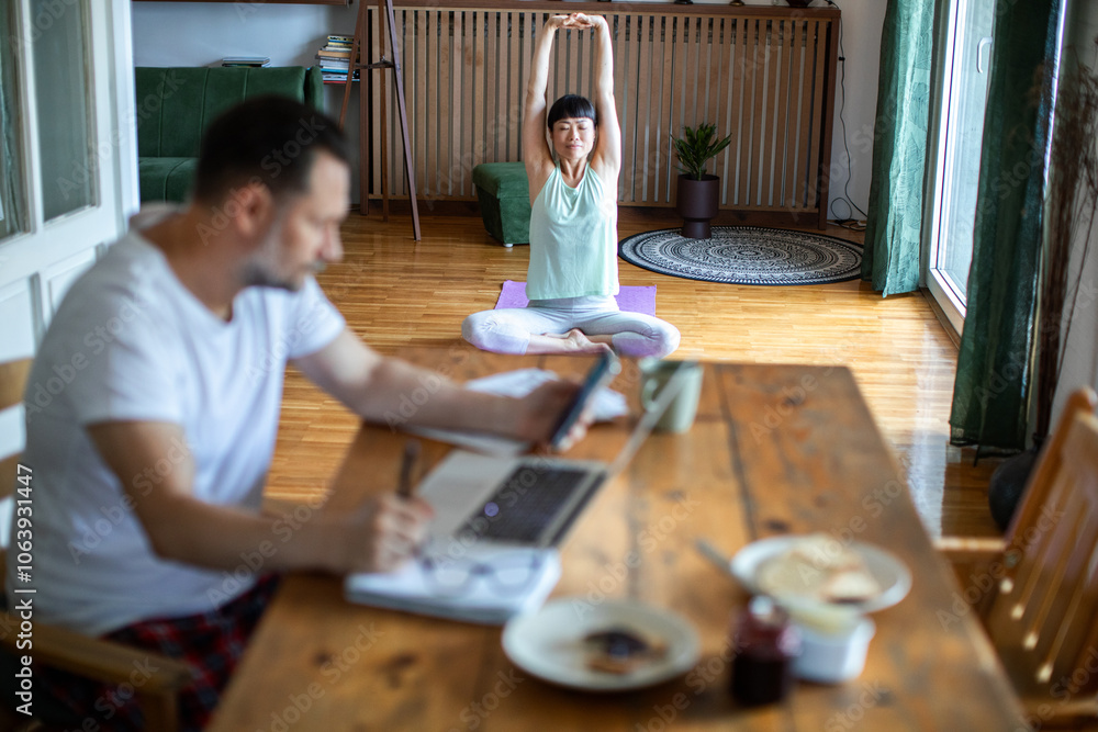 Woman doing morning yoga while man works on laptop at home Woman doing morning yoga while man works on laptop at home