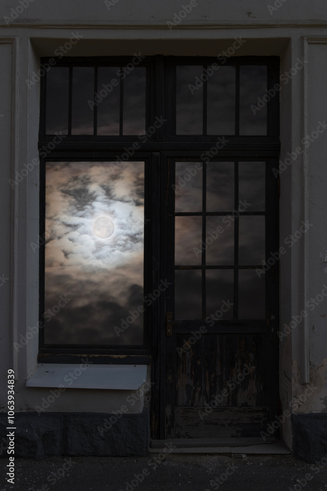 Fototapeta premium View of the full moon among the clouds through a closed window