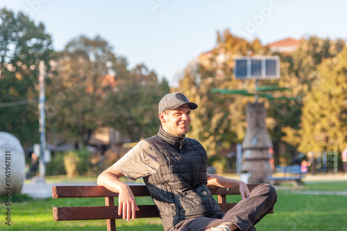 A cheerful man is sitting alone in the park on the bench and enjoying the autumn sun	