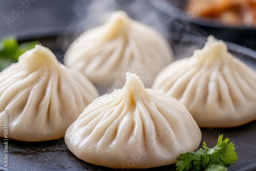 Four steaming, white dumplings with pleats on a black plate.