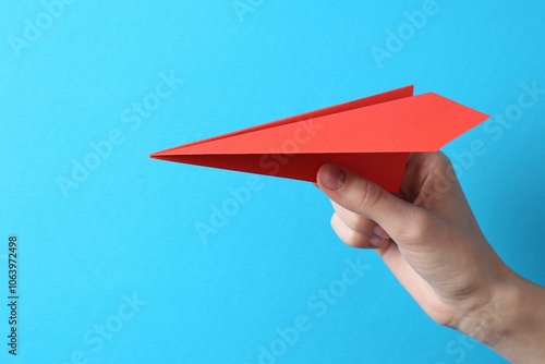 Woman with handmade paper plane on light blue background, closeup