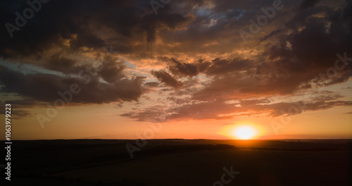 Bright colorful sunset sky with setting sun and vibrant clouds over dark landscape