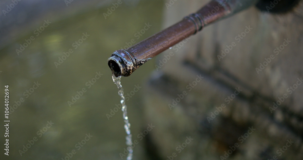 Close-up of an old metal faucet dripping water into a fountain, slow motion at 800 fps, rustic and aged appearance, peaceful water flow in a public outdoor setting Close-up of an old metal faucet dripping water into a fountain, slow motion at 800 fps, rustic and aged appearance, peaceful water flow in a public outdoor setting