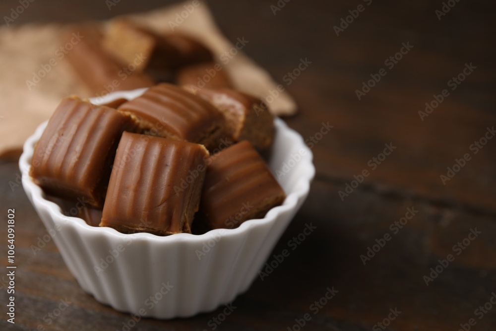 Tasty sweet caramel candies in bowl on wooden table, closeup Tasty sweet caramel candies in bowl on wooden table, closeup